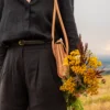 torebka-nr2-habaz-naturalna-stylizacja-kwiaty Detal naturalnej torebki Habaż na ramieniu i dłoń trzymająca bukiet żółtej wrotyczy.