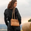 torebka-nr2-habaz-naturalna-stylizacja-z-na-tle-gor Modelka z naturalną torebką Habaż na ramieniu stoi na polu ze snopem siana w tle.