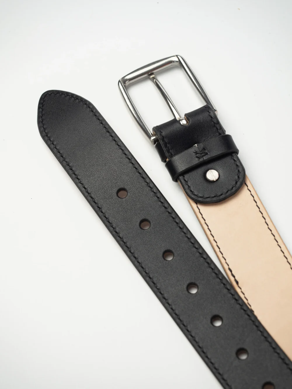 pasek-buttero-habaz-czarny-detal-dziurki Zbliżenie na czarny pasek Buttero z klamrą ze stali nierdzewnej. Widoczna jasna strona paska i wykończenie dziurek.