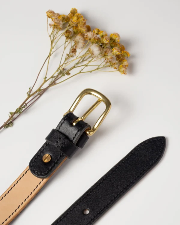 pasek-buttero-habaz-czarny-detal-kolor-mosiadz Pasek Buttero w dwóch kolorach: czarny z mosiężną klamrą i naturalny (jasny beż) bez klamry, z widocznym podwójnym szyciem i suchymi kwiatami.