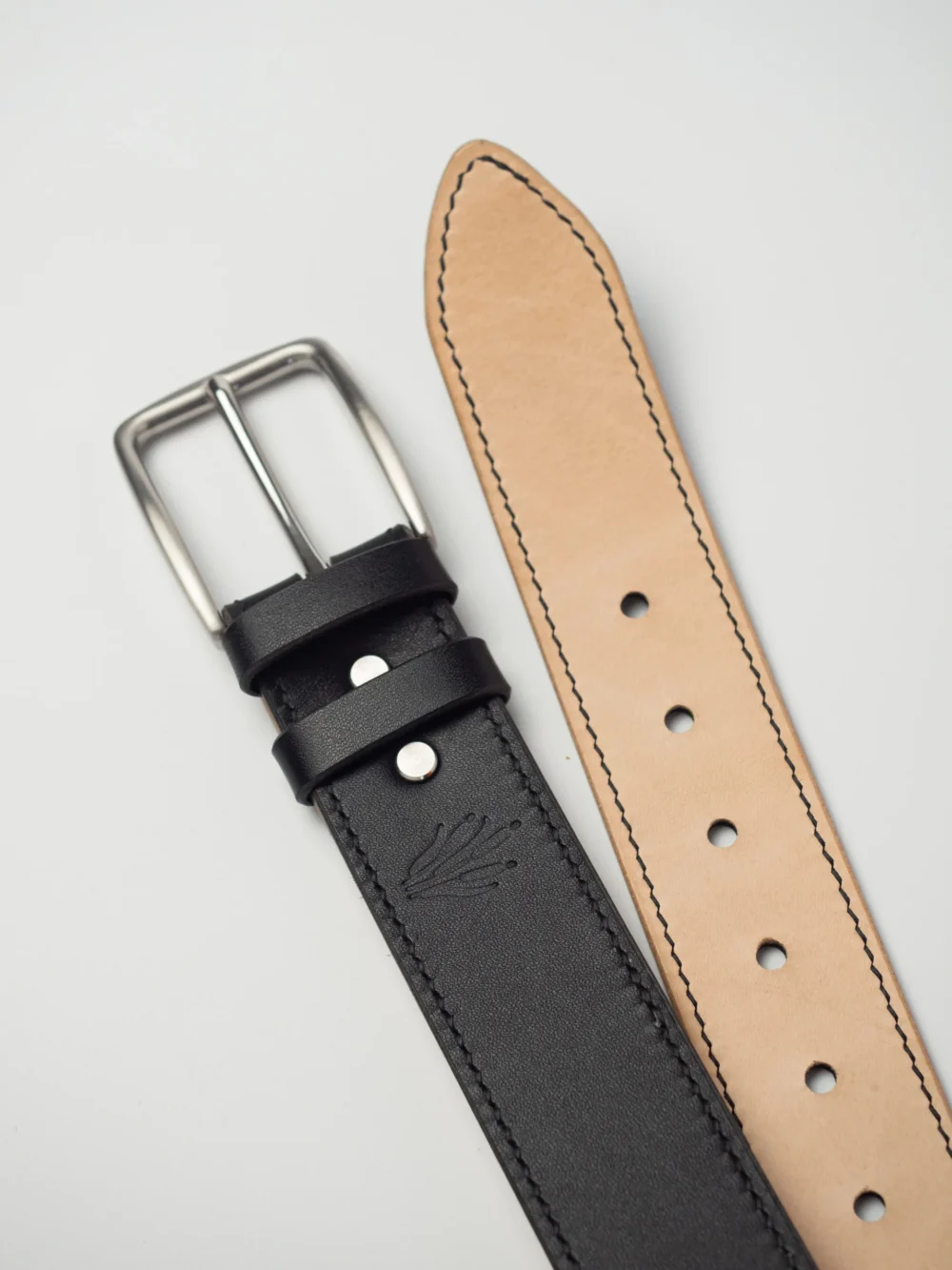 pasek-buttero-habaz-czarny-detal-logo Zbliżenie na czarny pasek Buttero ze stalową klamrą, widoczne wytłoczone logo Habaź.