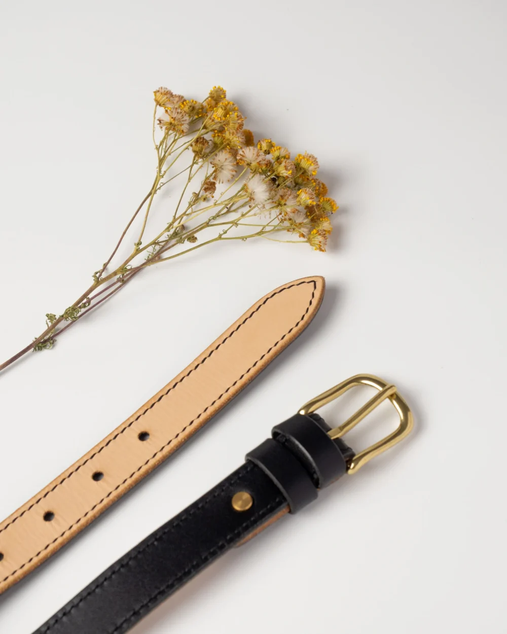 pasek-buttero-habaz-czarny-detal-mosiadz Zbliżenie na mosiężną klamrę czarnego paska Buttero, widoczny kontrast czarnej skóry i naturalnego spodu oraz dekoracyjne szycie.