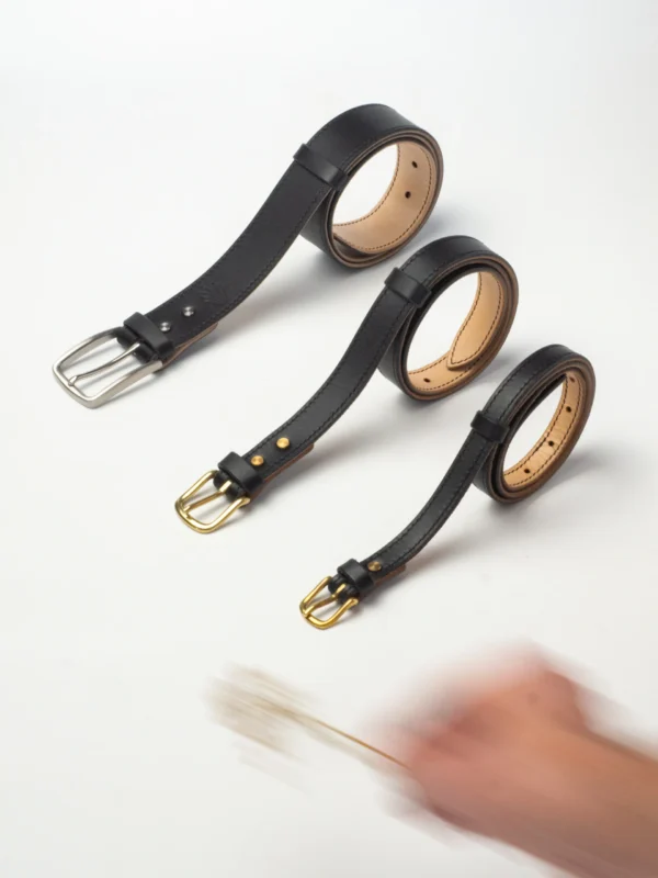 Trzy czarne paski Buttero, różnej szerokości (16, 25, 40 mm), w dynamicznym ujęciu z dłonią.