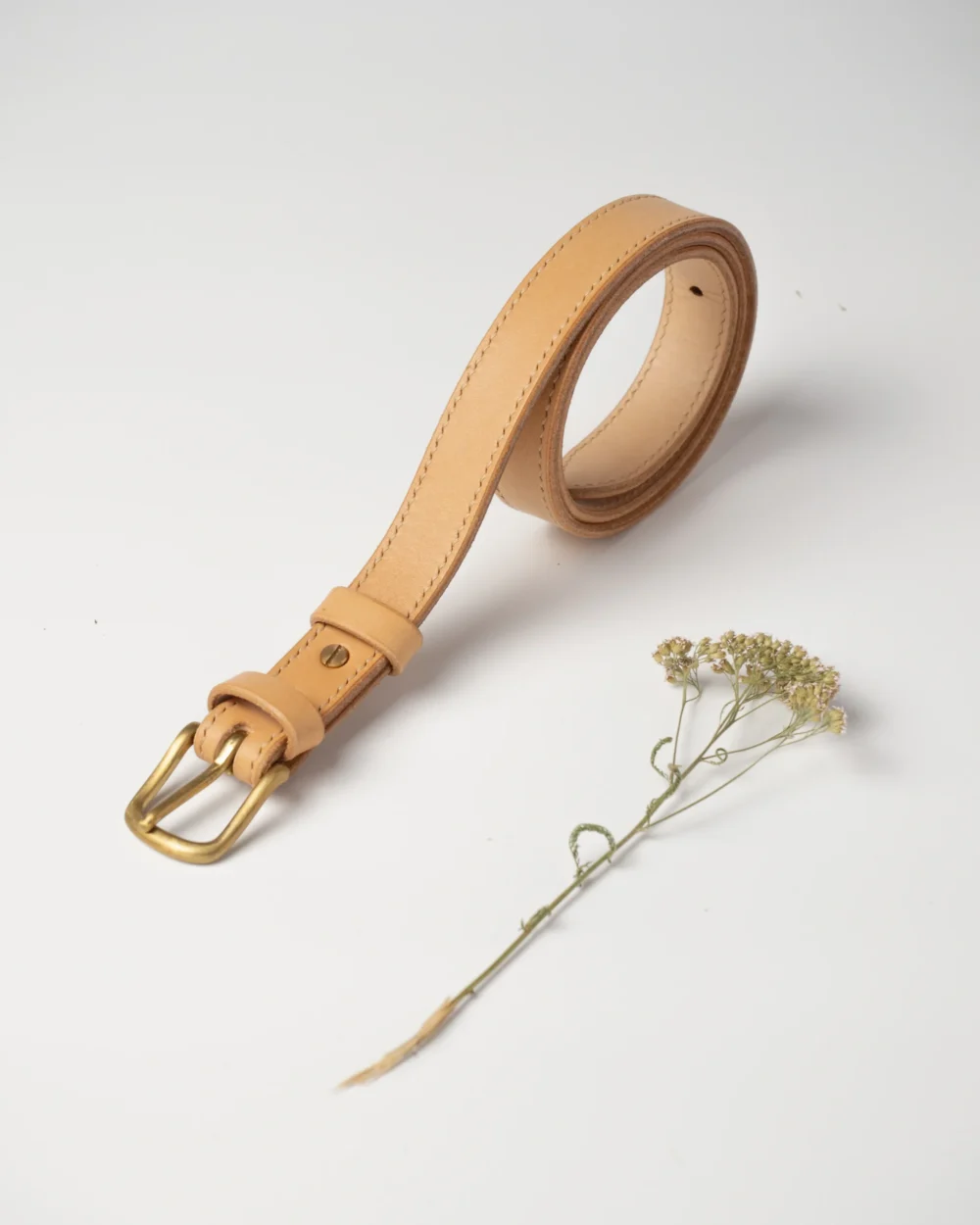 pasek-buttero-habaz-naturalny-produkt-zblizenie Skórzany pasek Buttero w kolorze naturalnym, zwinięty w spiralę, z widocznymi przeszyciami i mosiężną klamrą.