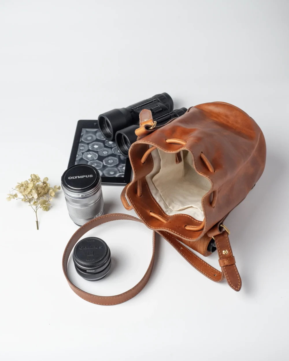 Karmelowa torebka Habaż, e-czytnik, lornetka i obiektyw na białym tle.