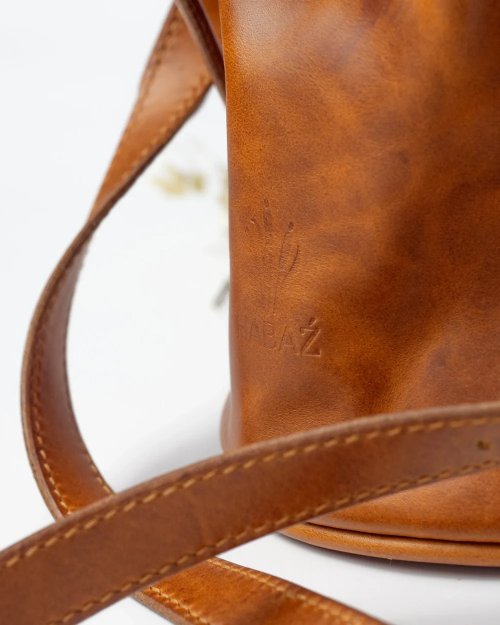 Zbliżenie na wytłoczone logo Habaż na karmelowej skórze torebki-worka, widoczny detal paska.