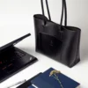 torebka-nr4-habaz-czarny-biuro-laptop Czarna torebka Shopper obok otwartego, czarnego laptopa i stosu notesów na białym biurku.