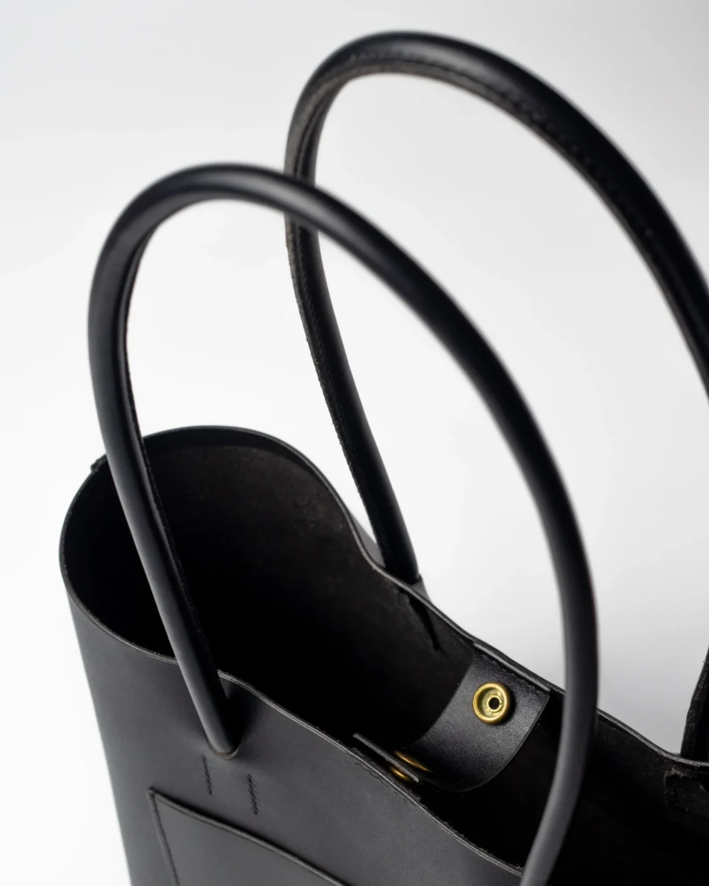 Zbliżenie na czarne skórzane uchwyty torebki Shopper i złoty zatrzask magnetyczny na środku.