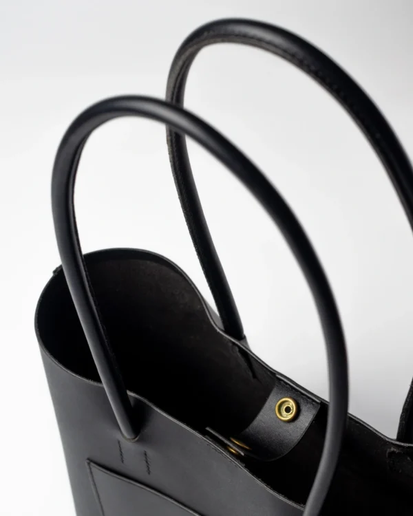 torebka-nr4-habaz-czarny-detal-zatrzask Zbliżenie na czarne skórzane uchwyty torebki Shopper i złoty zatrzask magnetyczny na środku.