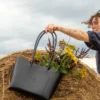 torebka-nr4-habaz-czarny-stylizacja-kwiaty Czarna skórzana torebka typu shopper (tote bag), wypełniona bukietem polnych kwiatów, trzymana przez osobę stojącą na stogu siana.