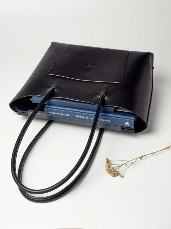 Widok z góry na otwartą, czarną torebkę Shopper, w której widać dwie niebieskie książki.