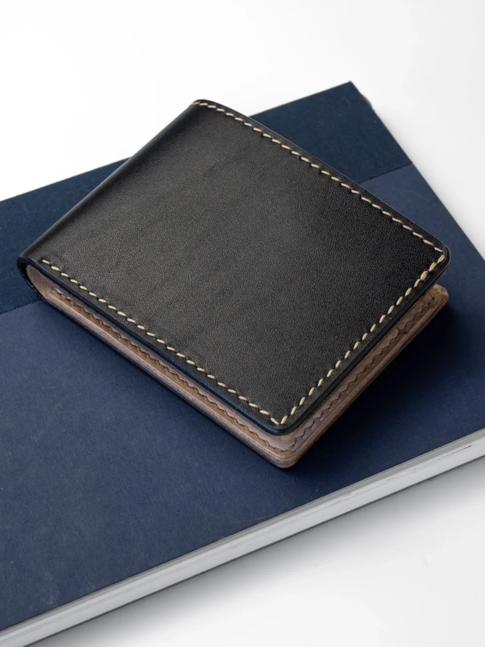 Kompaktowy, czarny portfel Habaź leżący na granatowym notatniku, ujęcie z góry. Widoczne beżowe, kontrastowe szycie.