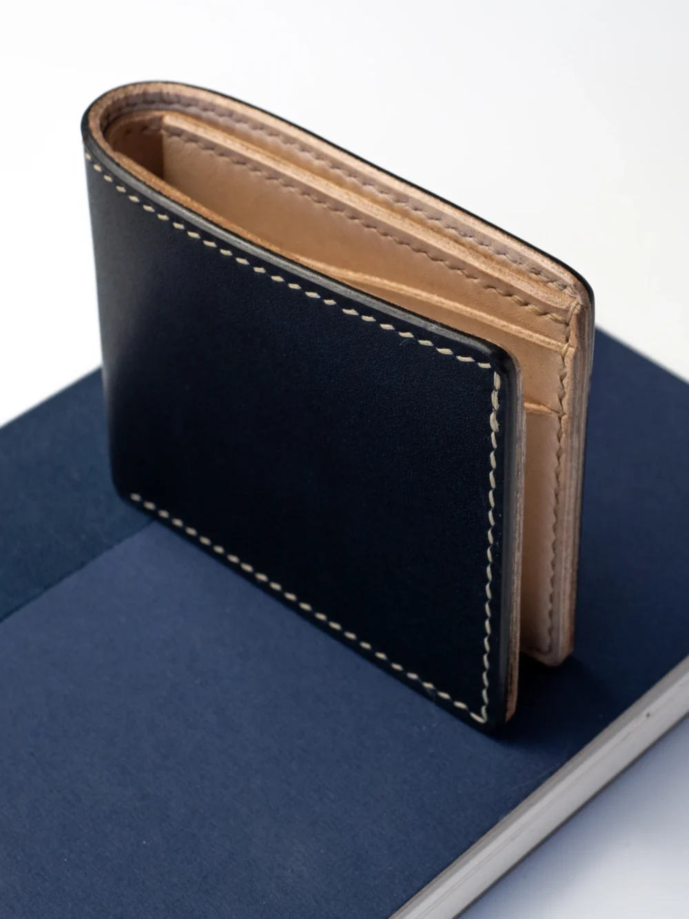 Czarny, skórzany portfel Habaź w pozycji półotwartej, stojący na granatowym notatniku. Widoczne kontrastowe beżowe szycie i jasne wnętrze.