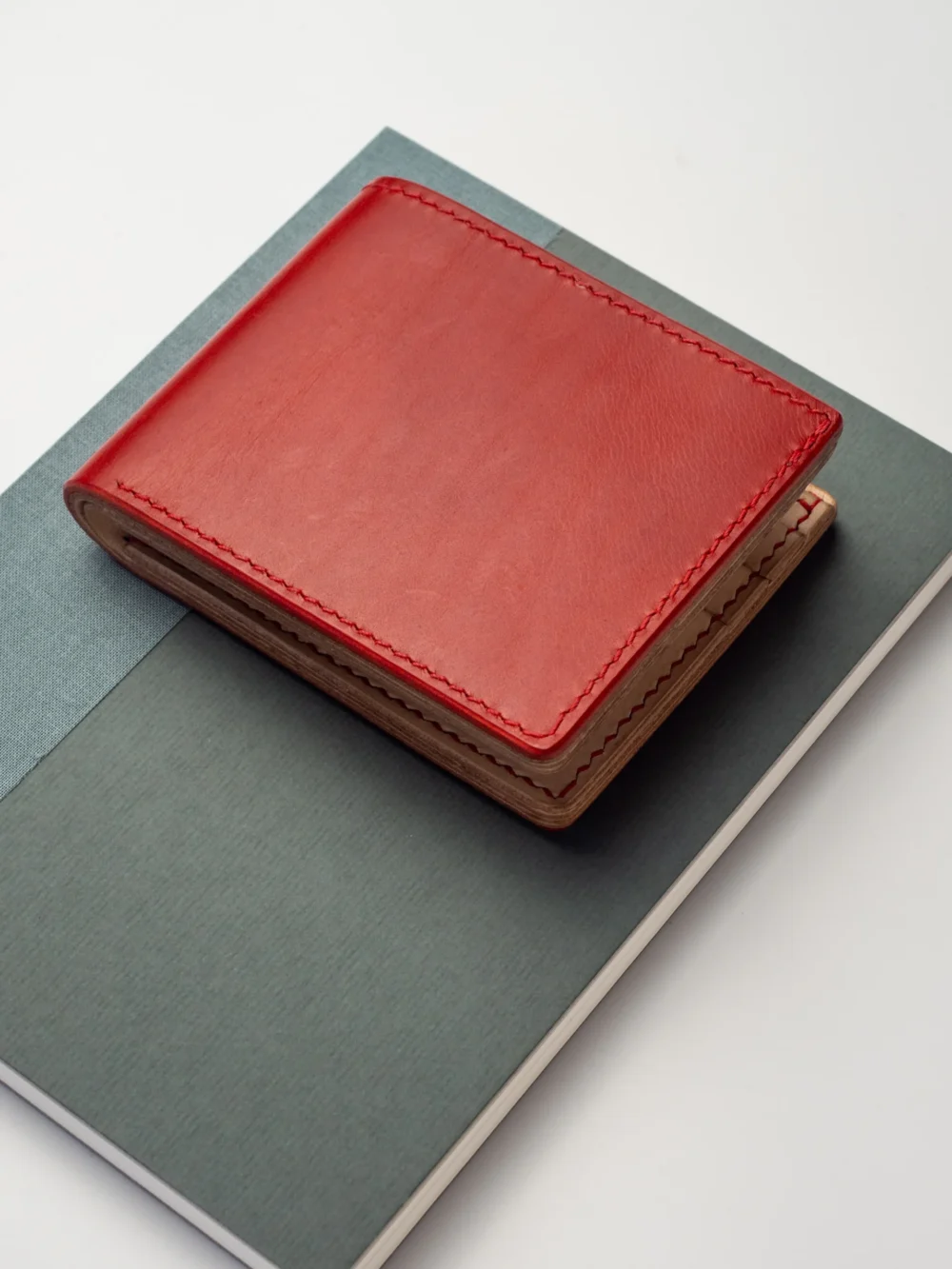 Kompaktowy, czerwony portfel Habaź położony na dwóch notatnikach (zielonym i niebieskim), z widocznym czerwonym szwem.