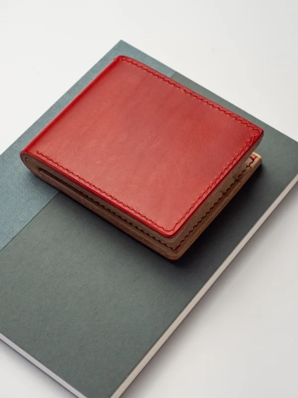 portfel-habaz-czerwony-góra-na-notatniku Kompaktowy, czerwony portfel Habaź położony na dwóch notatnikach (zielonym i niebieskim), z widocznym czerwonym szwem.
