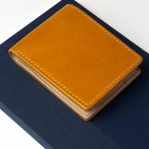 Musztardowy, skórzany portfel Habaź położony na granatowym notatniku, ujęcie z góry. Widoczne beżowe szycie i jasne wnętrze portfela.