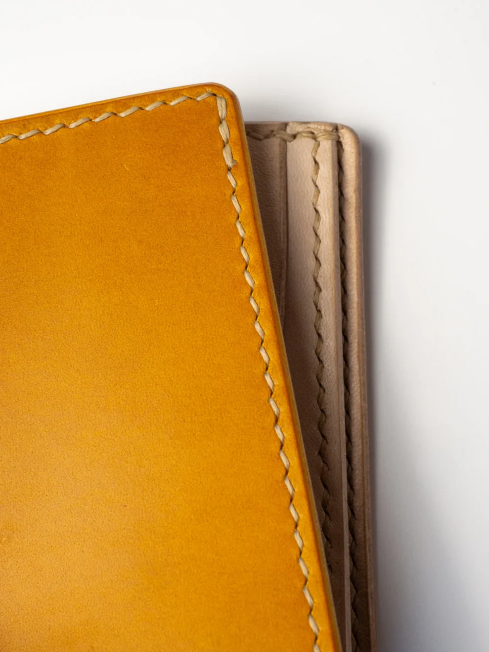 Bardzo bliskie ujęcie musztardowego portfela Habaź, koncentrujące się na krawędzi i prostym, beżowym szwie. Widoczna gładka tekstura skóry.