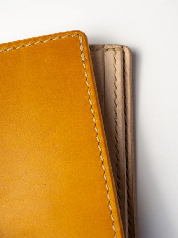 portfel-habaz-musztardowy-zbliżenie-szycie-krawędź Bardzo bliskie ujęcie musztardowego portfela Habaź, koncentrujące się na krawędzi i prostym, beżowym szwie. Widoczna gładka tekstura skóry.