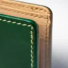 portfel-habaz-zielony-zbliżenie-bok-dwie-warstwy Ekstremalne zbliżenie na bok zielonego portfela Habaź, ukazujące dwie warstwy skóry - głęboką zieleń i naturalny beż, połączone beżowym szwem.