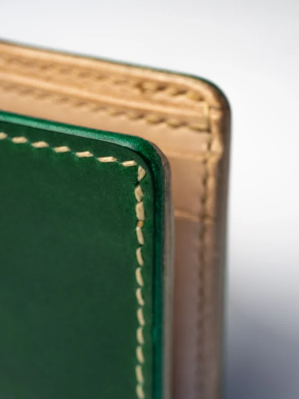 portfel-habaz-zielony-zbliżenie-bok-dwie-warstwy Ekstremalne zbliżenie na bok zielonego portfela Habaź, ukazujące dwie warstwy skóry - głęboką zieleń i naturalny beż, połączone beżowym szwem.