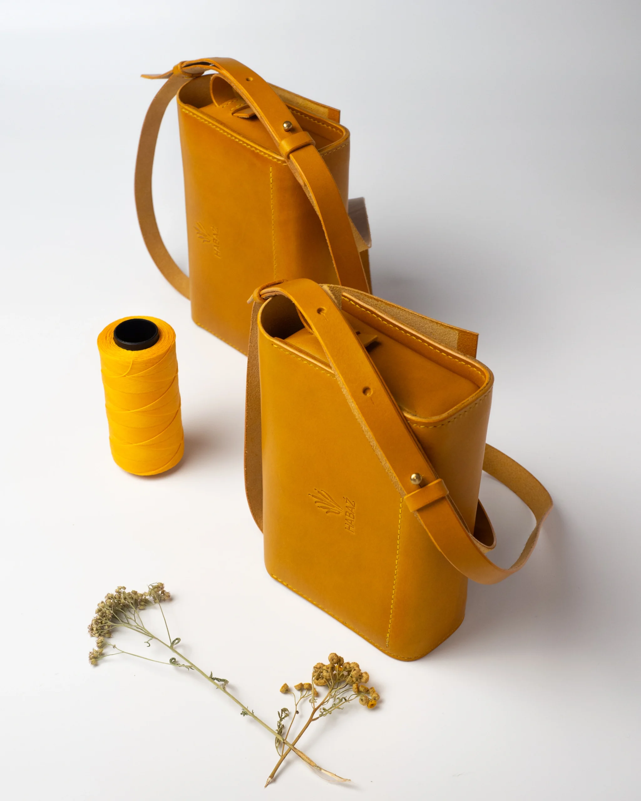 Dwie musztardowe torebki skórzane Habaż ustawione obok żółtej nici kaletniczej.
